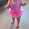 toddler, child, smiling, pink_tutu, leotard, barefoot, wooden_floor, sippy_cup, indoor, bedroom, happy, cute, young_child, person, standing, flooring, clothing, playful, joyful, home