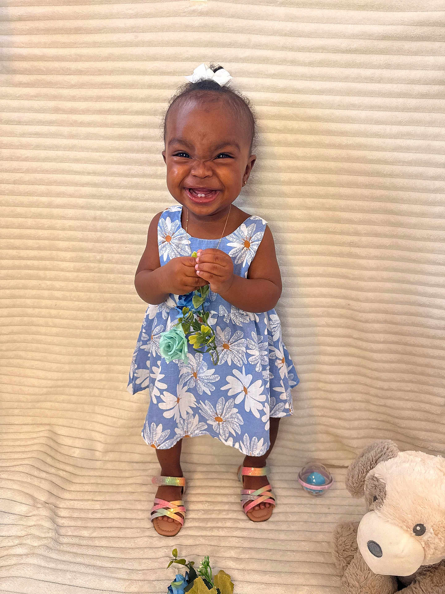 Jaydee joined the competition — help win amazing prizes! toddler, child, smiling, flower, dress, blue, floral_pattern, sandals, toy, plush_toy, teddy_bear, happy, indoors, cute, person, standing, young_child, accessory, joyful, background