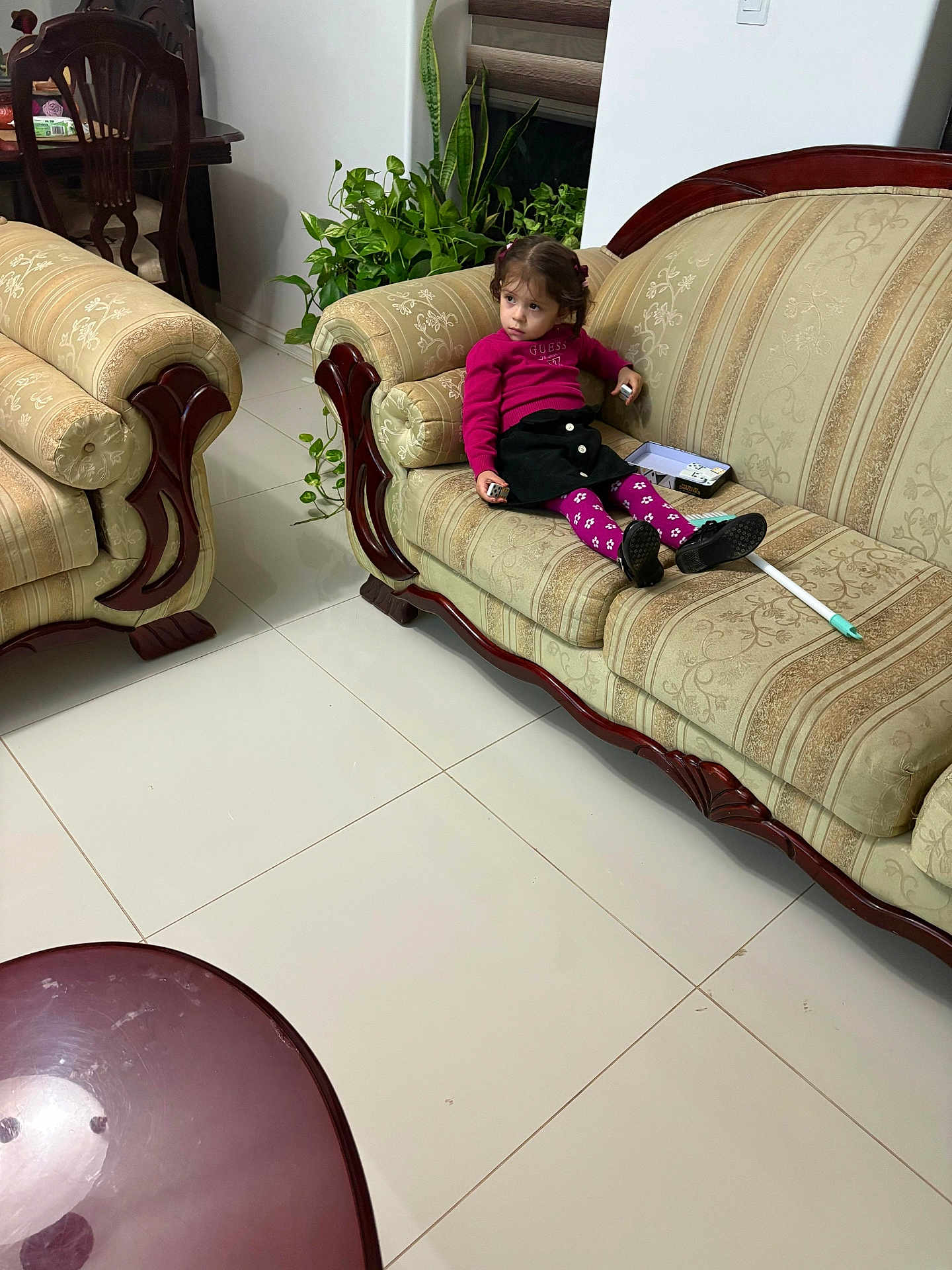 Bella joined the competition — help win amazing prizes! child, girl, sofa, living_room, plant, furniture, floor, tile, wood, clothing, pink_sweater, black_skirt, purple_tights, remote_control, indoor, home, seat, pensive, decor, toy