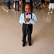 Lorenzo joined the competition — help win amazing prizes! child, flower, formal_clothing, indoor, people, standing, smiling, black_shoes, dress_pants, white_shirt, suspenders, hairstyle, event, crowd, floor, stroller, casual_clothing, background, portrait, person
