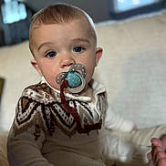 Maverick is registered to the contest to win money with this photo: baby, pacifier, blue_eyes, sweater, knitwear, indoor, child, cute, infant, portrait, soft_lighting, cozy, seated, face, expression, warm_colors, furniture, home, closeup, person