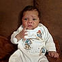 Grayson is registered to the contest to win money with this photo: baby, infant, child, pajamas, white_clothing, cartoon_print, couch, brown_couch, indoor, person, face, hand, sitting, expression, young_child, cute, portrait, furniture, home, soft_lighting