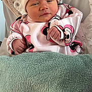 Inaya a rejoint le concours — aidez-le/la à gagner de superbes lots ! baby, infant, blanket, hat, clothing, cute, face, person, newborn, sleepwear, pink, white, green, soft, cozy, wrapped, resting, indoors, expression, mickey_mouse