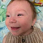 Noah is registered to the contest to win money with this photo: baby, smiling, close_up, face, child, striped_clothing, happy, infant, head, eyes, skin, cheeks, background, blanket, pattern, colorful, expression, person, portrait, cute