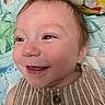 baby, smiling, close_up, face, child, striped_clothing, happy, infant, head, eyes, skin, cheeks, background, blanket, pattern, colorful, expression, person, portrait, cute