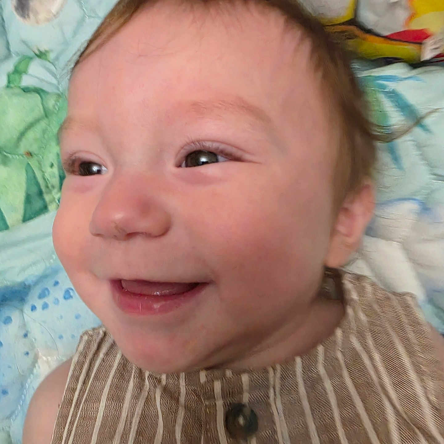 Noah is registered to the contest to win money with this photo: baby, smiling, close_up, face, child, striped_clothing, happy, infant, head, eyes, skin, cheeks, background, blanket, pattern, colorful, expression, person, portrait, cute