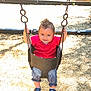 toddler, child, swing, playground, outdoor, sunlight, smiling, red_shirt, striped_pants, shoes, wood_chips, metal_chains, fence, play_area, baby, happy, young_child, casual_clothing, daytime, park