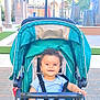 Antony is registered to the contest to win money with this photo: baby, stroller, child, smiling, outdoor, sunny, urban, pavement, green, striped_shirt, pink_shorts, footwear_free, happy, seatbelt, toy, hand, face, person, daylight, park