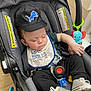 baby, sleeping, car_seat, cap, bib, clothing, toy, pacifier, footwear, infant, child, cute, indoor, seatbelt, black_pants, white_shoes, blue, red, yellow, peaceful