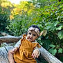 baby, child, headband, dress, outdoor, bench, wood, greenery, nature, portrait, cute, smile, curly_hair, skin, feet, hand, sitting, young_child, casual_clothing, daylight