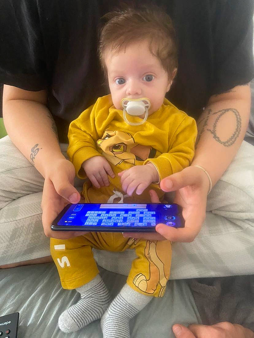 Ezio participe au concours pour gagner de l'argent avec cette photo : baby, child, couch, electric_blue, face, fictional_character, finger, fun, gadget, gesture, hand, happy, human_leg, lap, person, sitting, snapshot, t_shirt, thigh, thumb