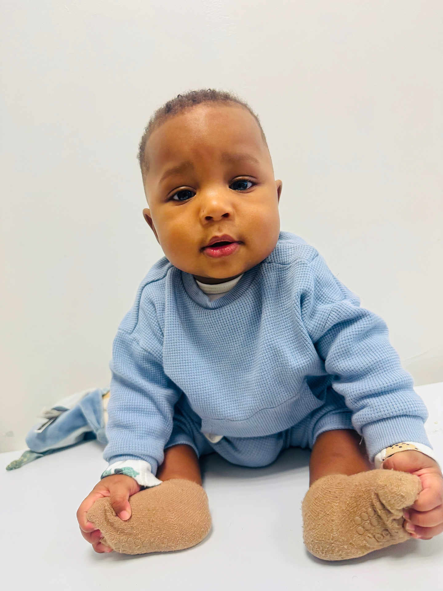Hakim participe au concours pour gagner de l'argent avec cette photo : baby, blue_sweater, booties, child, clothing, curious_expression, cute, eyes, face, feet, hands, indoor, infant, portrait, sitting, skin, soft_lighting, table_surface, toddler, white_background
