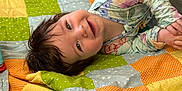 Mary Grace is registered to the contest to win money with this photo: baby, child, smiling, quilt, patchwork, colorful, floral_outfit, lying_down, indoor, happy, cute, infant, playpen, blanket, person, young_child, face, head, portrait, cozy