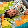 baby, child, smiling, quilt, patchwork, colorful, floral_outfit, lying_down, indoor, happy, cute, infant, playpen, blanket, person, young_child, face, head, portrait, cozy