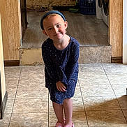 Madelyn joined the competition — help win amazing prizes! child, girl, smiling, blue_headband, navy_dress, pink_slippers, indoor, tiled_floor, wallpaper, laundry_basket, home, cute, standing, portrait, floor_tiles, headwear, footwear, young_child, casual_clothing, happy