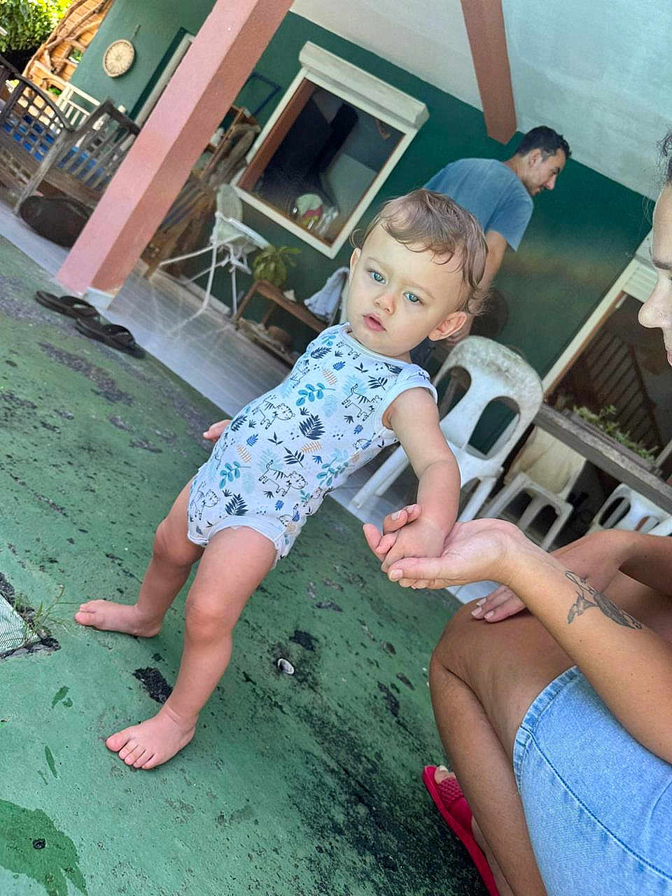 Luka a rejoint le concours — aidez-le/la à gagner de superbes lots ! toddler, child, baby, hand_holding, walking, outdoor, floor, person, adult, clothing, chair, tattoo, footwear, green_floor, window, table, plant, slippers, casual, expression