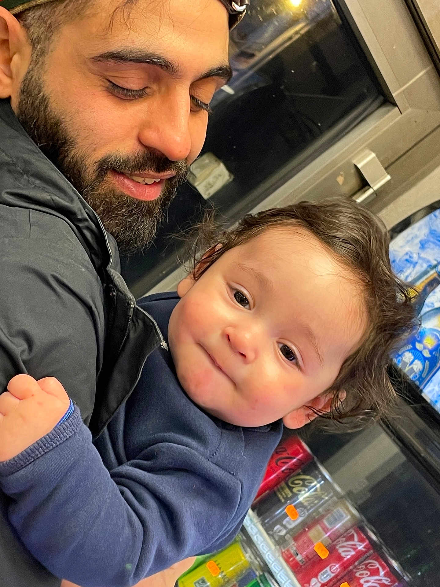 Yasser Aylan participe au concours pour gagner de l'argent avec cette photo : baby, man, adult_male, beard, smile, cuddling, jacket, window, soda_cans, beverages, indoor, public_transport, holding, close_up, cute, curly_hair, cheeks, face, portrait, candid