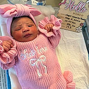 Nayeli joined the competition — help win amazing prizes! newborn, baby, pink_clothing, knitted_outfit, headband, bow, hospital, bassinet, blanket, sign, text, infant, person, cute, sleepy, portrait, closeup, skin, hand, face