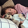 girl, dog, sleeping, couch, blanket, pillow, remote_control, indoors, cozy, resting, pet, child, comfort, relaxation, casual_clothing, brown_hair, fur, snuggling, peaceful, home