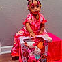 Ophelia joined the competition — help win amazing prizes! toddler, child, girl, pink_clothing, toy_box, hello_kitty, plush_toys, hair_buns, colorful_hair_ties, bracelet, sitting, indoor, wooden_floor, gray_wall, valentine, candy, packaging, pink_stool, curious_expression, bright_colors