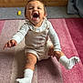 Remi is registered to the contest to win money with this photo: baby, child, laughing, sitting, carpet, sock, wooden_wall, indoor, cute_outfit, happy, portrait, smiling, one_person, infant, playful, white_clothing, floor, warm_lighting, deer_design, expression