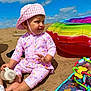 toddler, child, beach, sand, sunhat, swimsuit, toy, inflatable_ring, bottle, sunny, outdoor, play, colorful, blue_sky, clouds, smiling, sitting, barefoot, summer, fun