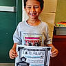 child, boy, smiling, award, certificate, tshirt, school, indoor, brick_wall, green_door, missing_tooth, proud, holding, portrait, young, casual_clothing, class_photo, education, student, person
