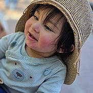 Eshaal is registered to the contest to win money with this photo: baby, blue_shirt, blurred_background, child, close_up, clothing, eyes, face, hair, happy, infant, joy, outdoor, photography, portrait, seated, smiling, sun_hat, toddler, woven_hat