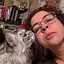 affection, books, cat, close_up, cozy, curly_hair, decor, face, giraffe_painting, glasses, gray_cat, home, indoor, nuzzling, pet, portrait, sentimental_message, shelf, wall_art, woman