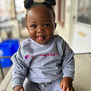Ariyah joined the competition — help win amazing prizes! child, toddler, smiling, tongue_out, hair_buns, gray_clothing, sweatshirt, sweatpants, portrait, outdoor, porch, table, person, cute, happy, sitting, playful, face, skin, fashion
