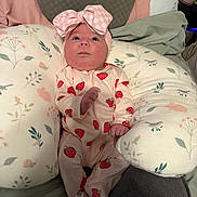 Layla is registered to the contest to win money with this photo: baby, infant, newborn, headband, bow, onesie, strawberry_print, nursing_pillow, floral_pattern, pillow, bed, blanket, face, eyes, hand, fingers, adult_leg, indoor, portrait, cute