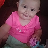 Heavenly joined the competition — help win amazing prizes! baby, child, pink_shirt, toy, hair_tie, couch, indoor, person, smile, face, infant, cute, playful, holding, seated, young_child, looking, hand, bright_clothing, expression