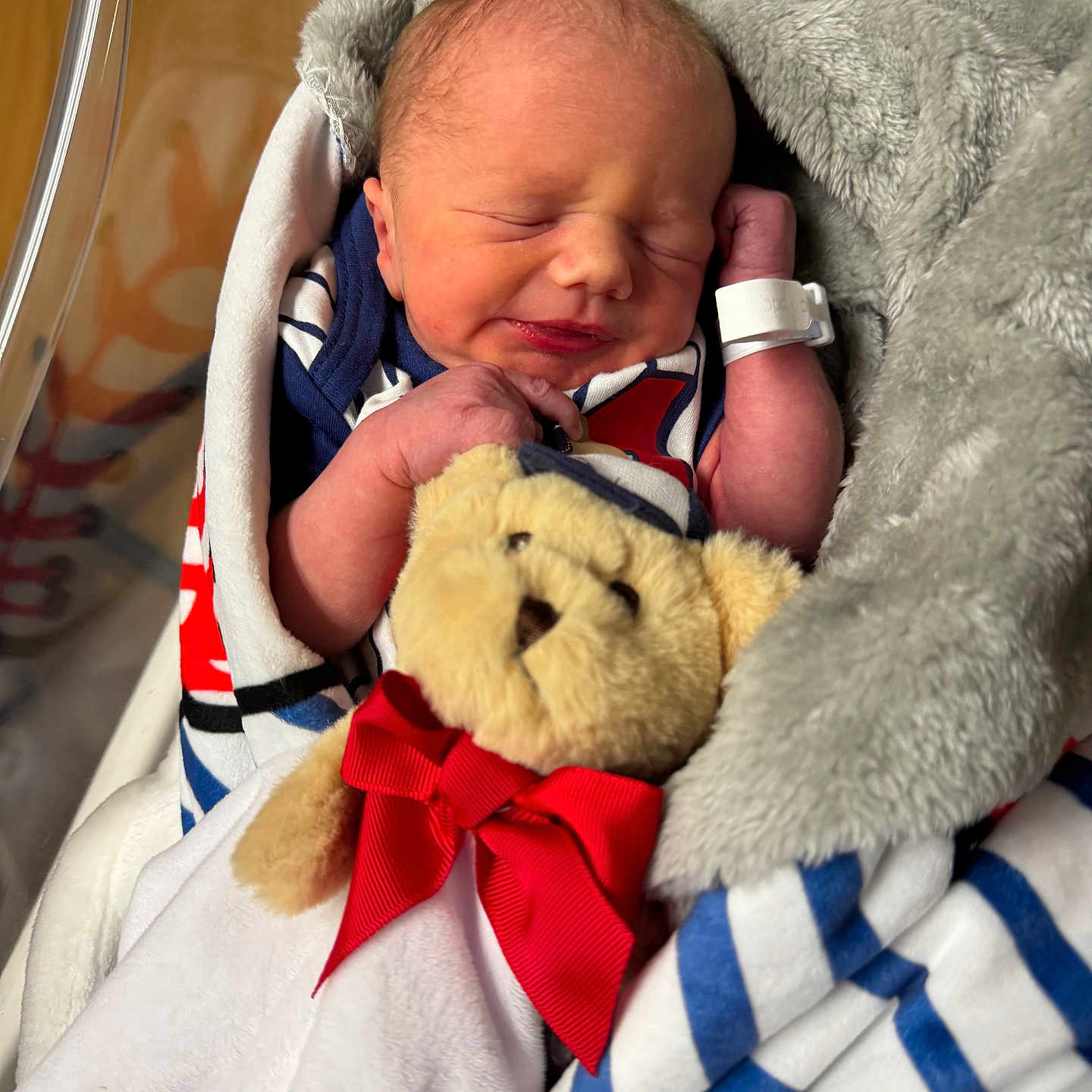 Jericho is registered to the contest to win money with this photo: newborn, baby, sleeping, blanket, teddy_bear, plush_toy, red_bow, hospital, infant, wrapped, cute, peaceful, swaddled, soft_texture, cradle, child, portrait, indoors, wearing_clothes, tiny