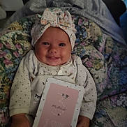 Malya participe au concours pour gagner de l'argent avec cette photo : baby, smiling, infant, headwrap, milestone_card, blanket, floral, cute, cozy, clothing, happy, portrait, child, hand, sitting, indoors, face, person, newborn, soft_lighting