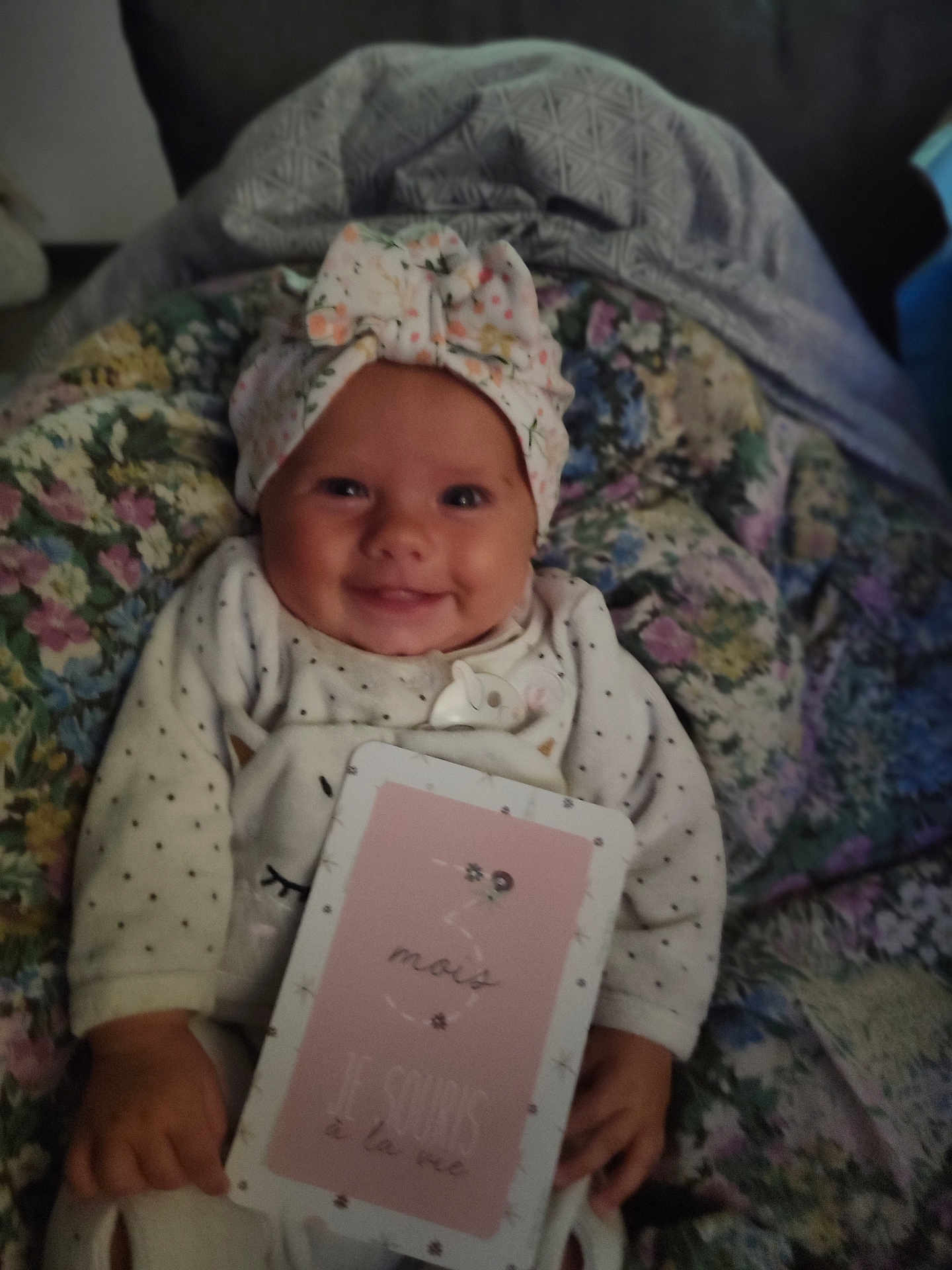 Malya participe au concours pour gagner de l'argent avec cette photo : baby, smiling, infant, headwrap, milestone_card, blanket, floral, cute, cozy, clothing, happy, portrait, child, hand, sitting, indoors, face, person, newborn, soft_lighting