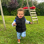 Noah a rejoint le concours — aidez-le/la à gagner de superbes lots ! black_vest, blue_jeans, bushes, casual_clothing, child, cloudy_sky, curly_hair, daytime, grass, greenery, happy, lawn, nature, outdoor, playground, running, sneakers, swing_set, toddler, wooden_structure