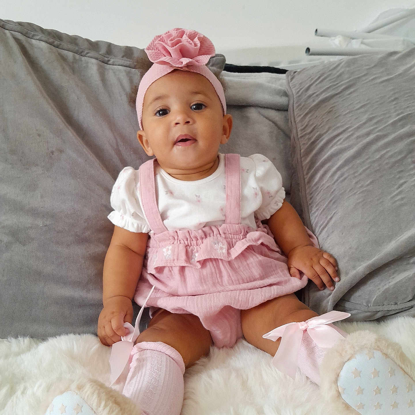Hasiley-Rae is registered to the contest to win money with this photo: baby, bows, child, comfortable, couch, cozy, cute, flower, fluffy_rug, headband, indoor, infant, person, pillows, pink_clothing, portrait, sitting, smiling, socks, soft_texture