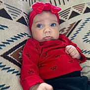 Presley joined the competition — help win amazing prizes! baby, blue_eyes, bow, child, closeup, cozy, curious_expression, cute, face, fist, headband, indoors, infant, patterned_cushion, portrait, red_clothing, sitting, soft_lighting, textile_pattern, young