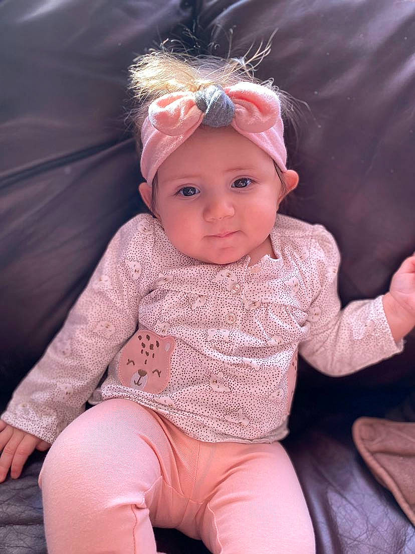 Ava Mae is registered to the contest to win money with this photo: baby, blond, cheek, child, child_model, ear, face, fashion_accessory, hair_accessory, head, headband, headgear, person, pink, sitting, skin, sleeve, toddler