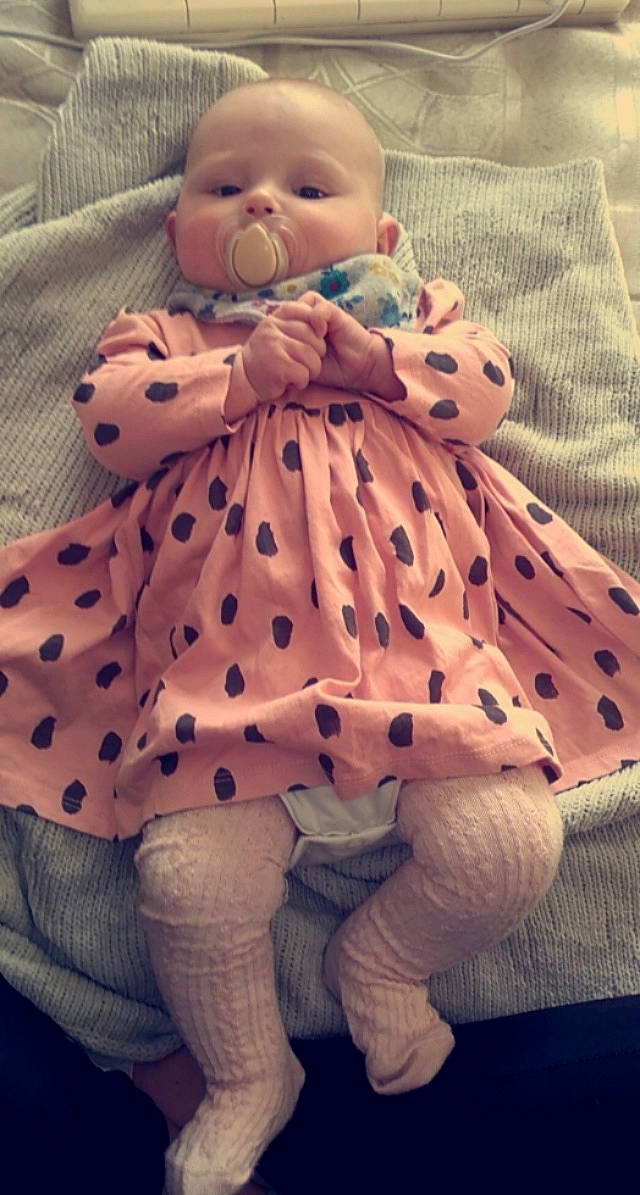 Darcie is registered to the contest to win money with this photo: baby, baby_toddler_clothing, child, comfort, day_dress, dress, happy, human_body, human_leg, linens, one_piece_garment, pattern, person, sitting, skin, sleeve, textile, thigh, toddler, toy