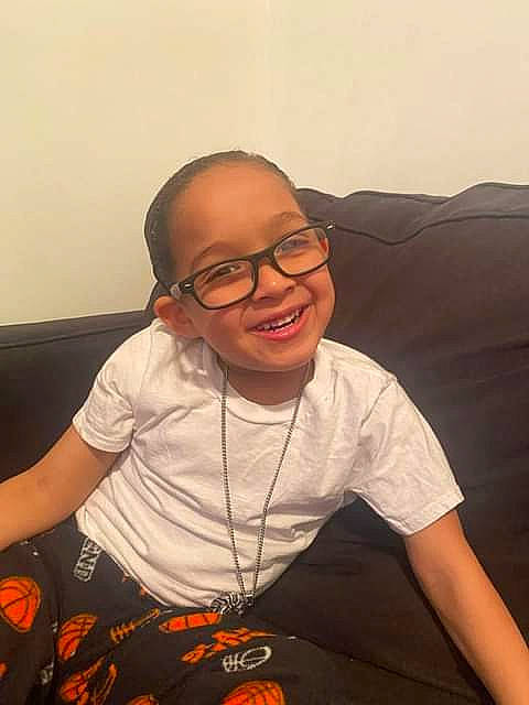 Joshua is registered to the contest to win money with this photo: child, comfort, cool, couch, elbow, eyewear, finger, flooring, fun, glasses, happy, joy, mouth, orange, person, room, sitting, sleeve, smile, t_shirt