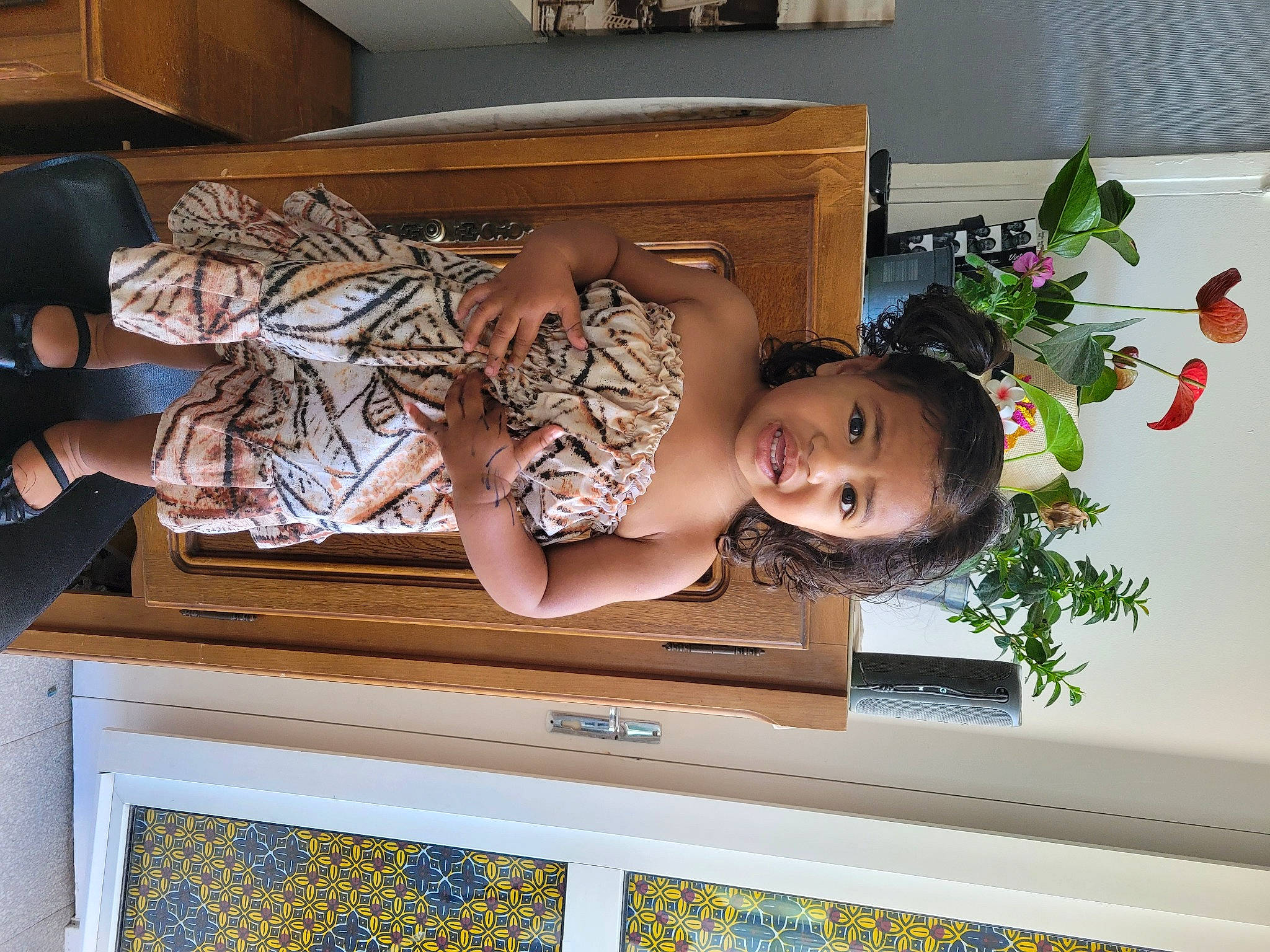 Akila a rejoint le concours — aidez-le/la à gagner de superbes lots ! baby_toddler_clothing, child, comfort, dress, flower, happy, hardwood, home, houseplant, human_leg, person, plant, rectangle, room, sitting, smile, thigh, toddler, window, wood