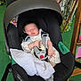 baby, sleeping, car_seat, blanket, pacifier, infant, child, straps, black, green_carpet, wooden_furniture, plants, indoor, clothing, peaceful, resting, toddler, person, comfort, seat