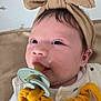 Ellie is registered to the contest to win money with this photo: baby, pacifier, headband, close_up, infant, face, skin, eyes, clothing, bed, pattern, animal_print, soft_toy, yellow, beige, expression, cute, child, adorable, indoors