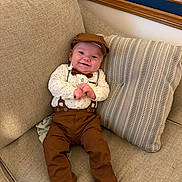Elijah is registered to the contest to win money with this photo: baby, child, smile, couch, pillow, clothing, hat, bow_tie, suspenders, feet, happy, indoor, person, seated, fabric, furniture, cute, infant, portrait, relaxed