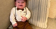 Elijah is registered to the contest to win money with this photo: baby, smiling, child, couch, pillow, clothing, hat, bow_tie, suspenders, pants, barefoot, indoors, portrait, happy, person, furniture, seated, cute, fabric, home