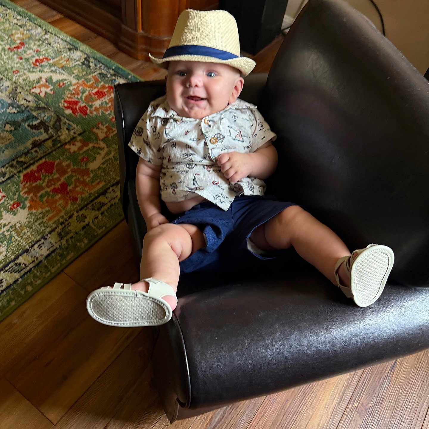 Elijah is registered to the contest to win money with this photo: baby, child, hat, smile, chair, indoor, shirt, shorts, footwear, leather, floor, rug, wood, happy, sitting, person, cute, playful, home, furniture