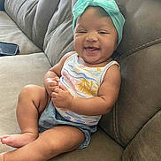 Kenalaya joined the competition — help win amazing prizes! baby, smiling, sitting, couch, headband, bow, clothing, happy, infant, person, skin, arm, leg, foot, furniture, indoor, cute, child, portrait, relaxed