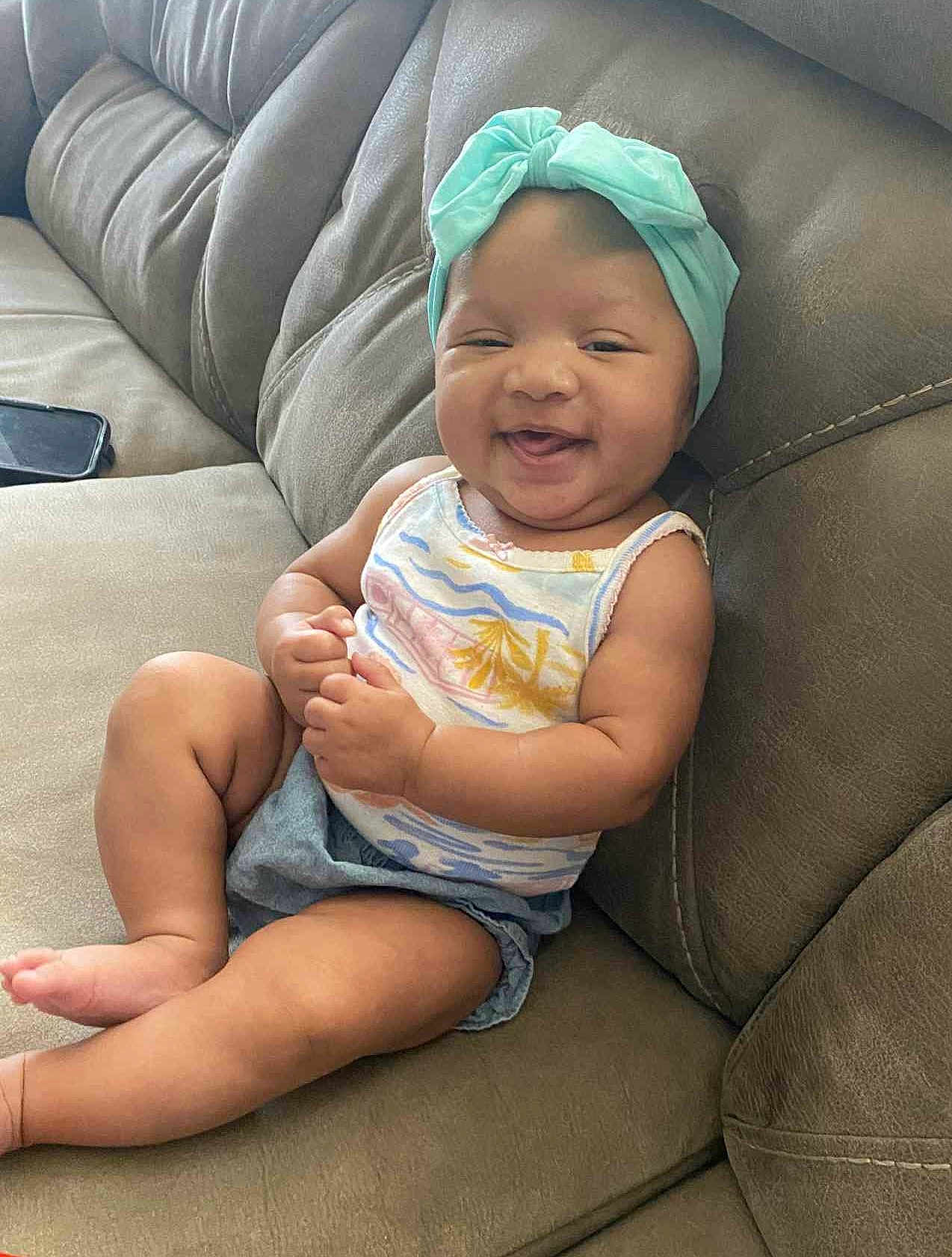 Kenalaya joined the competition — help win amazing prizes! baby, smiling, sitting, couch, headband, bow, clothing, happy, infant, person, skin, arm, leg, foot, furniture, indoor, cute, child, portrait, relaxed