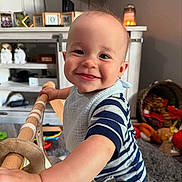 Kane is registered to the contest to win money with this photo: baby, child, smile, striped_clothing, bib, toy, living_room, carpet, wooden_toy, face, happy, person, infant, play, furniture, indoors, cute, expression, warm_lighting, home